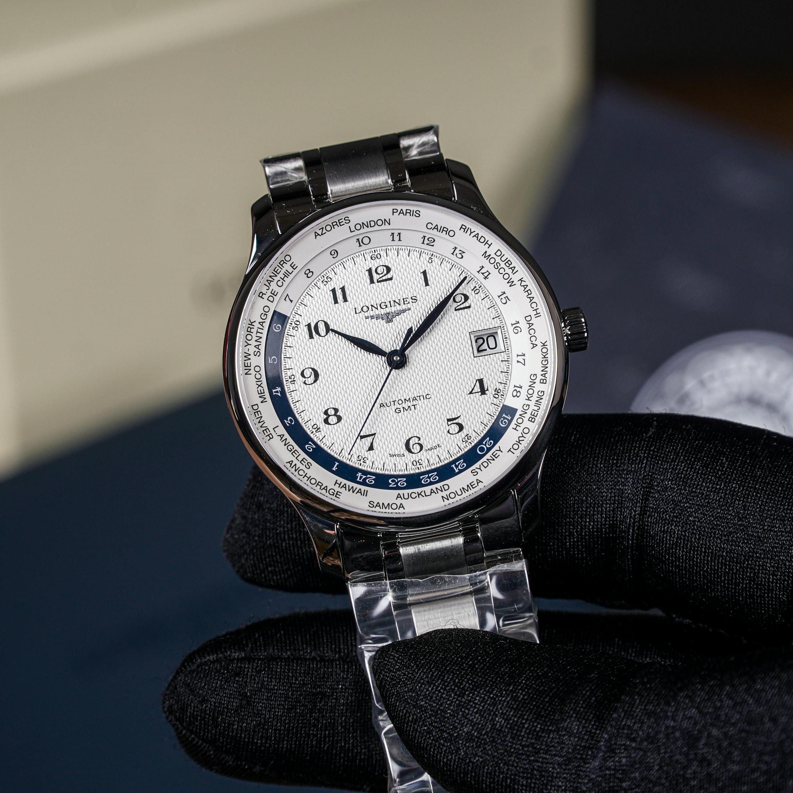 Close-up of a sophisticated silver wristwatch with world time feature, held by a gloved hand.